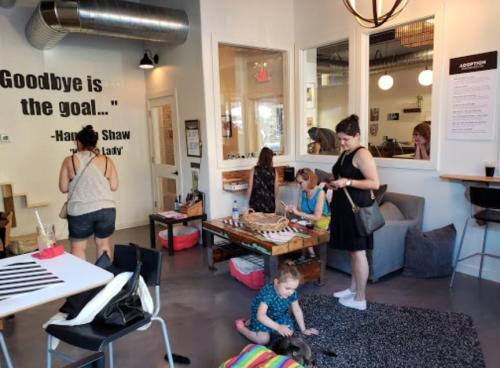 A cozy interior of a shop with people interacting, a child playing on the floor, and a quote on the wall.