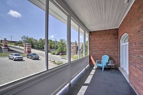 A porch with a blue chair and potted plant, overlooking a street with parked cars and greenery in the background.