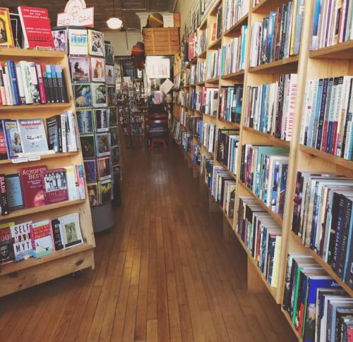 A cozy bookstore aisle lined with wooden shelves filled with books, leading to a bright, inviting space.