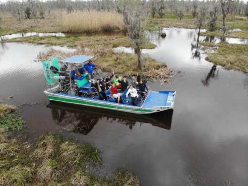 A group of people on an airboat in a swampy area, surrounded by water and tall grasses.