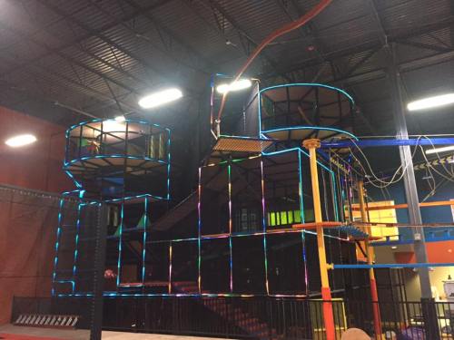 Brightly lit indoor play structure with multiple levels and colorful lights, featuring climbing areas and slides.