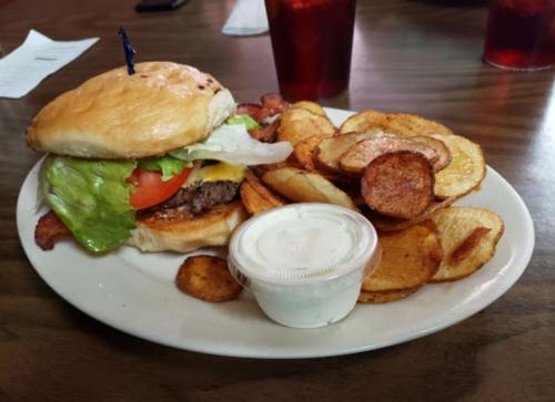 A juicy burger with lettuce, tomato, and cheese, served with crispy potato wedges and a side of dipping sauce.