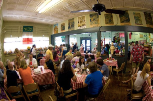 A busy restaurant filled with people dining at tables with checkered tablecloths and colorful decor on the walls.