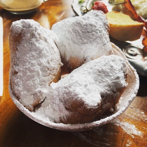 A bowl of three powdered sugar-covered beignets on a wooden table.