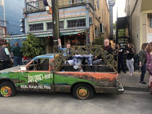 A colorful truck with "Jacques-Imo's Real Nawlins Food" sign, parked outside a lively restaurant with people around.