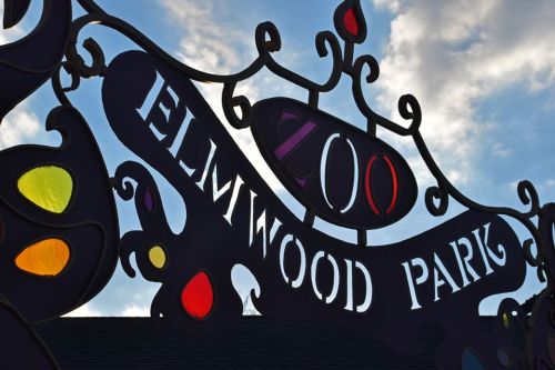 Colorful sign for Elmwood Park Zoo against a cloudy sky.