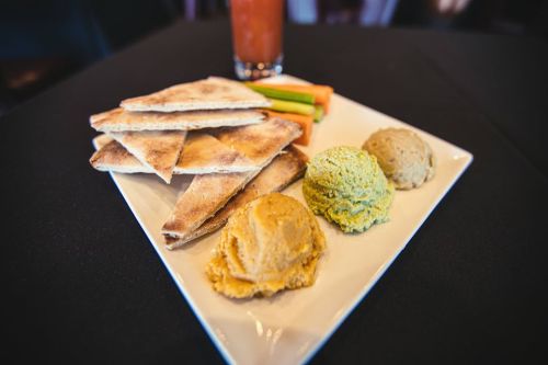 A plate with toasted pita bread and three dips: hummus, green spread, and a yellow spread, alongside carrot sticks.