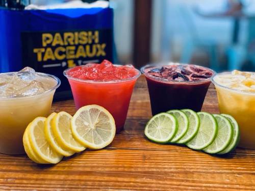 Three colorful drinks in cups with ice, surrounded by lemon and lime slices on a wooden table.