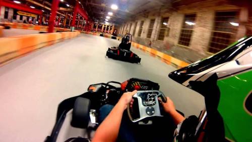 A view from a go-kart racing on an indoor track, with another kart ahead in the distance.