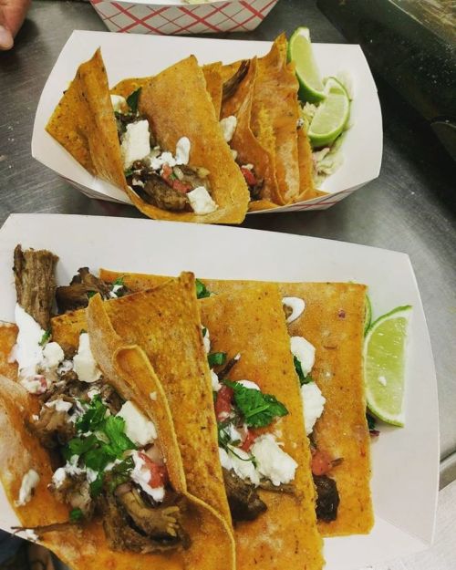 Two trays of tacos filled with beef, cheese, pico de gallo, and garnished with lime wedges.