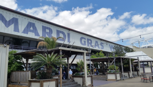 Exterior of a building with "Mardi Gras" signage, featuring palm trees and a blue sky with clouds.