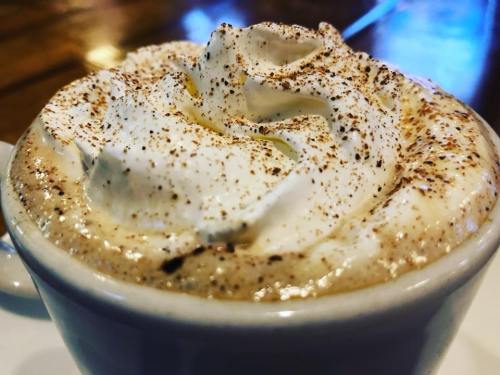 A close-up of a creamy coffee topped with whipped cream and a sprinkle of cocoa powder.