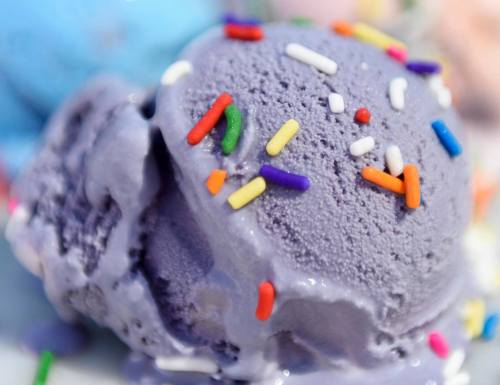 A close-up of a scoop of purple ice cream topped with colorful sprinkles.