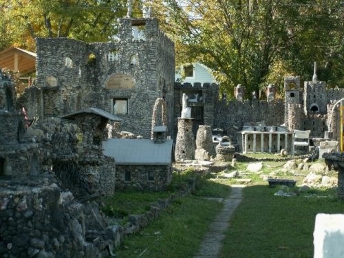 A whimsical stone castle landscape with various structures and a grassy path, surrounded by trees.