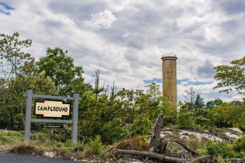 A sign reading "Campground" with a tower in the background, surrounded by trees and a cloudy sky.