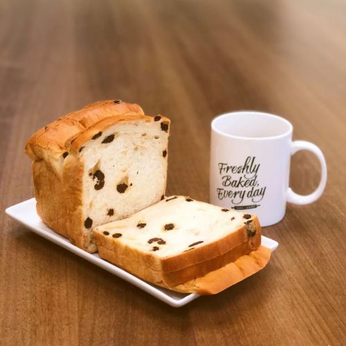 A loaf of chocolate chip bread on a plate next to a coffee mug that says "Freshly Baked. Every day."
