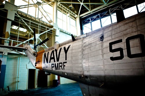 A close-up of a Navy helicopter inside a hangar, showcasing its metallic body and tail rotor.