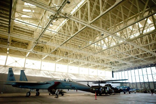 Interior of an aircraft hangar featuring various military helicopters and planes under a high ceiling.