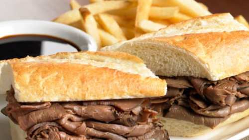 A close-up of a roast beef sandwich on a toasted bun, served with a side of fries and dipping sauce.