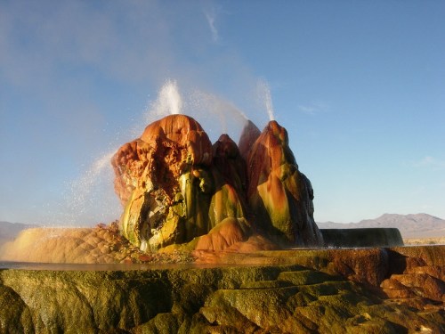Colorful mineral formations erupting water in a natural hot spring landscape under a clear blue sky.