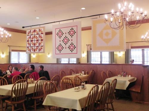 A cozy restaurant interior with wooden tables, chairs, and colorful quilt art hanging from the ceiling.