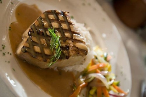 Grilled fish fillet on a bed of rice, garnished with herbs, served with a colorful vegetable medley.