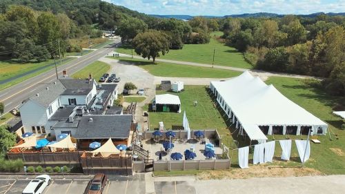 Aerial view of a venue with a large white tent, outdoor seating, and green fields in the background.