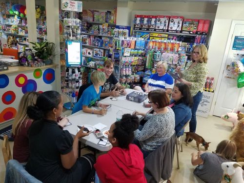 A group of people gathered around a table in a colorful toy store, engaged in a creative activity.