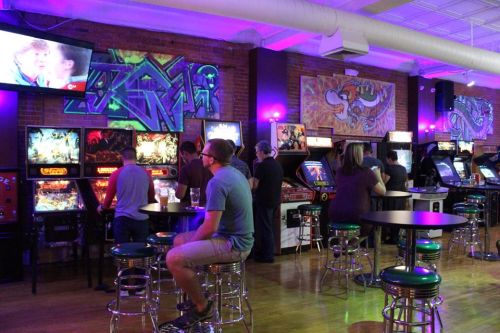 A vibrant arcade with people playing pinball and video games, colorful graffiti on the walls, and a cozy atmosphere.