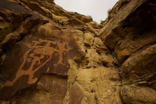 Petroglyphs carved into a rocky cliff, depicting human figures with outstretched arms against a natural stone background.