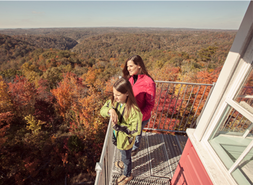 Two women stand on a lookout platform, enjoying a vibrant autumn landscape filled with colorful trees.
