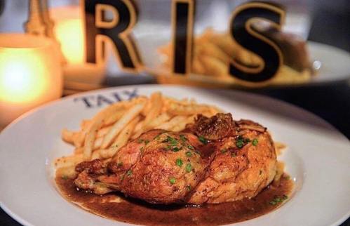 A plate of roasted chicken with gravy, garnished with herbs, served alongside golden French fries.