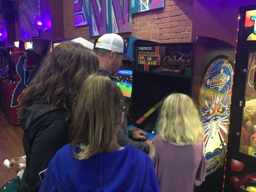 A group of four people playing classic arcade games in a colorful gaming venue.