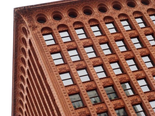 Close-up of a historic red brick building with ornate detailing and large windows, showcasing architectural design.