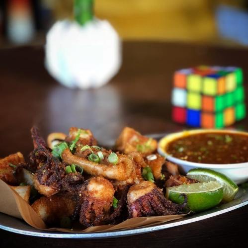 A plate of crispy fried octopus with lime wedges and dipping sauce, next to a Rubik's Cube.