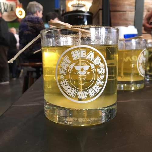 A glass of yellow liquid with a label reading "Fat Head's Brewery" on a table, with people in the background.