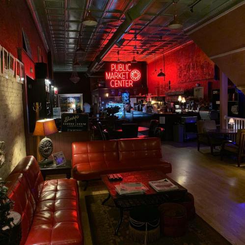 Cozy interior of a bar with red lighting, vintage furniture, and a neon "Public Market Center" sign.