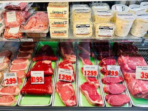 A display case filled with various cuts of meat, including steaks and sausages, with price tags visible.