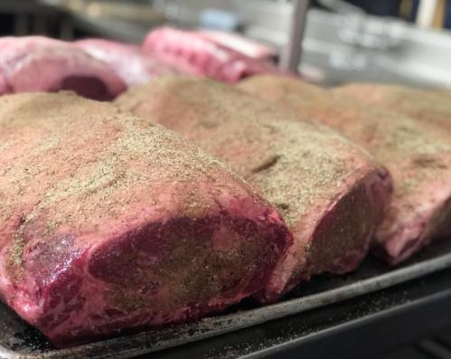Raw cuts of beef seasoned with spices, arranged on a metal tray in a kitchen setting.