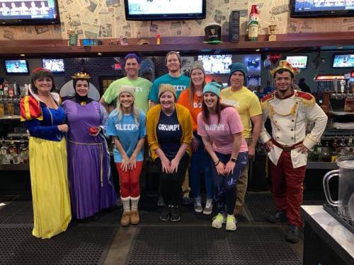 A group of people dressed as Snow White and the Seven Dwarfs, posing together in a bar setting.