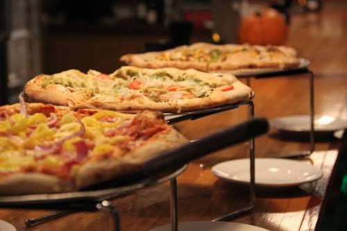 Three pizzas on a wooden table, featuring various toppings, with a pumpkin in the background.