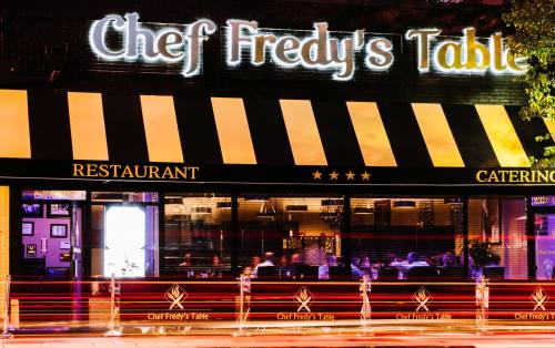 A restaurant exterior with a sign reading "Chef Fredy's Table," featuring outdoor seating and illuminated at night.
