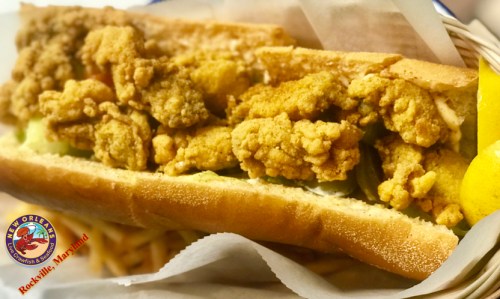 A close-up of a po' boy sandwich filled with crispy fried shrimp, served in a toasted baguette with lemon.
