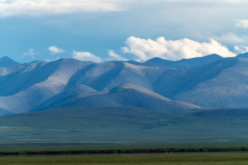 A panoramic view of rolling mountains under a cloudy sky, with varying shades of blue and green in the landscape.