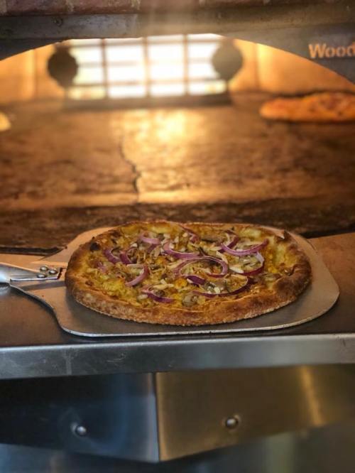 A freshly baked pizza with toppings, resting on a pizza peel in a wood-fired oven.