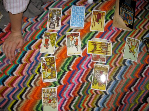 A colorful blanket with tarot cards laid out, including various suits and orientations, and a hand resting nearby.