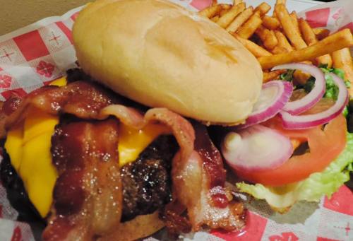 A juicy cheeseburger topped with bacon, served with fries and fresh vegetables on a red checkered plate.