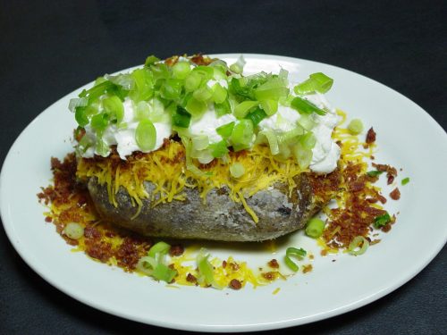 A loaded baked potato topped with cheese, sour cream, and green onions, served on a white plate.