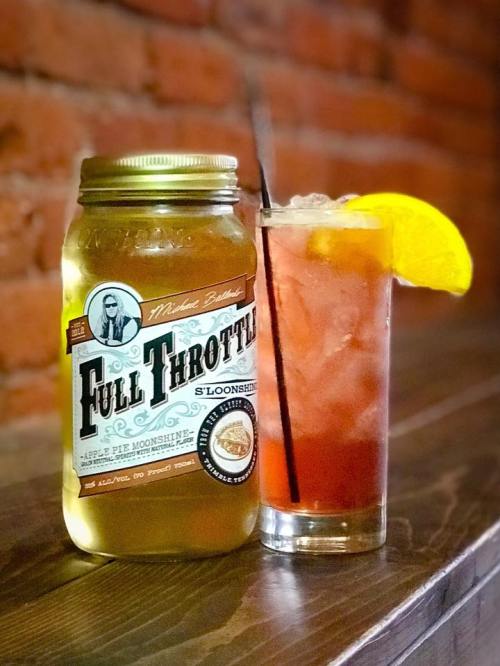 A jar of Full Throttle apple pie moonshine next to a glass of iced tea garnished with a lemon slice.