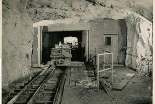 A vintage mine tunnel with a small train on tracks, leading to a dark opening in the rock.